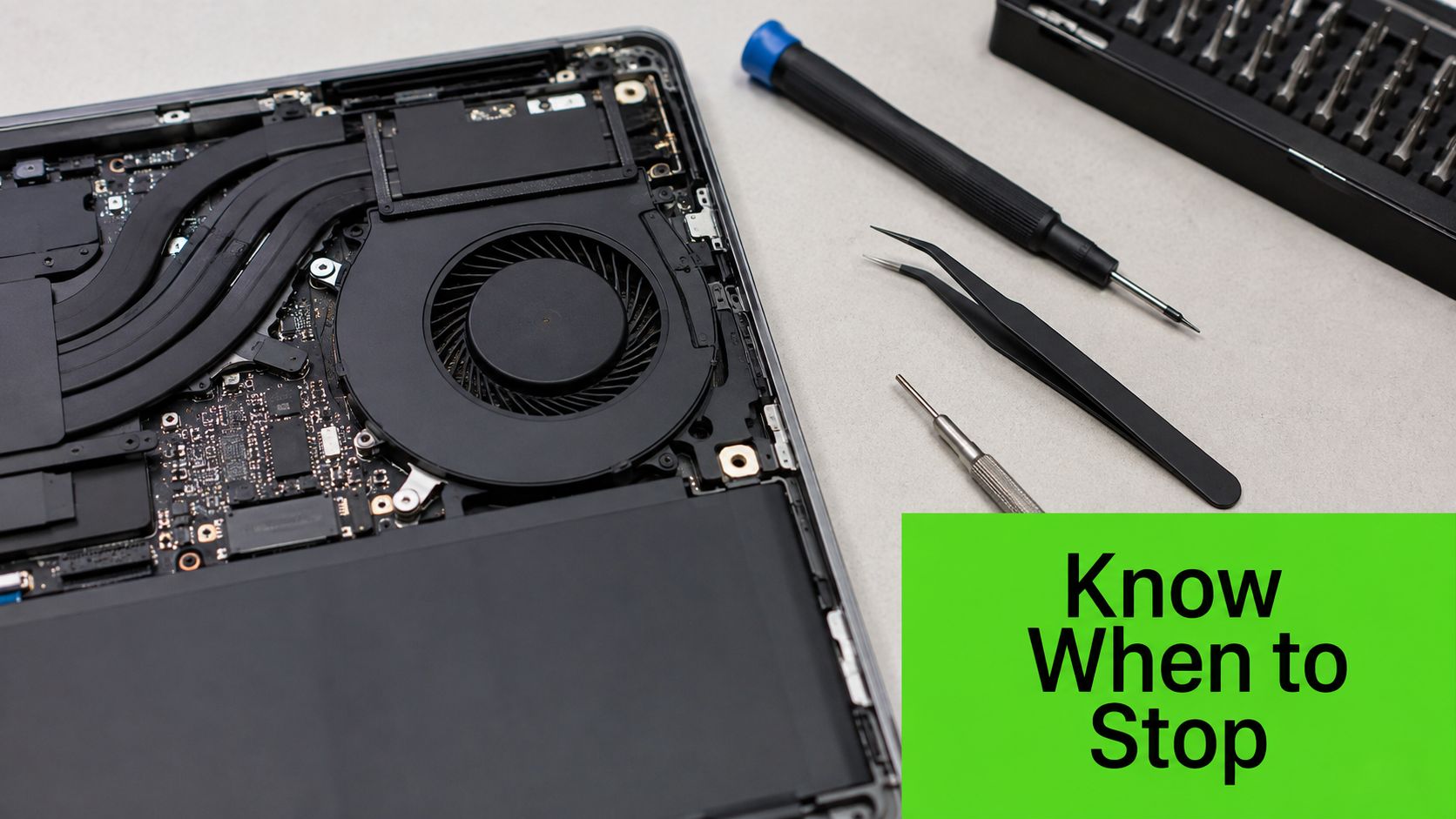 An open laptop with internal cooling system exposed, along with specialized repair tools on a table.